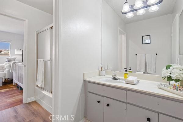 bathroom featuring vanity, hardwood / wood-style flooring, and bath / shower combo with glass door