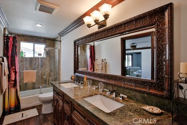full bathroom with ornamental molding, tiled shower / bath, vanity with extensive cabinet space, toilet, and dual sinks