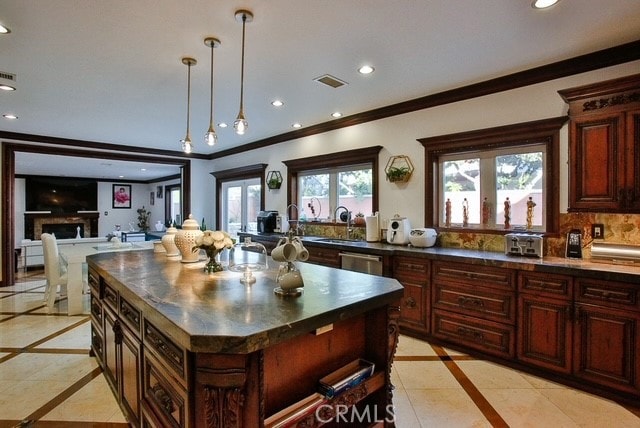 kitchen featuring hanging light fixtures, ornamental molding, a kitchen island, backsplash, and light tile floors