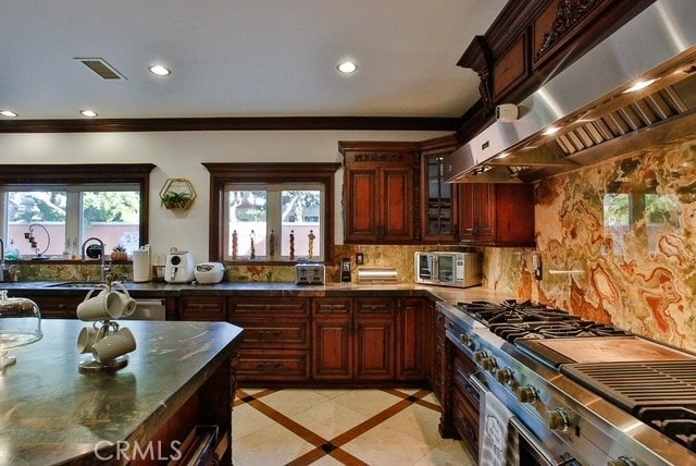 kitchen with light tile flooring, tasteful backsplash, stainless steel range, wall chimney exhaust hood, and ornamental molding