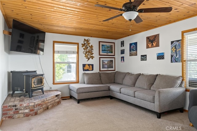 carpeted living room with wood ceiling, ceiling fan, a wealth of natural light, and a wood stove