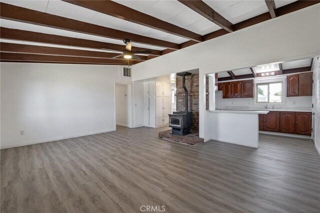 unfurnished living room featuring vaulted ceiling with beams, ceiling fan, a wood stove, and light hardwood / wood-style flooring