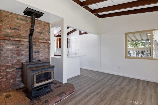 unfurnished living room featuring a wood stove, hardwood / wood-style floors, lofted ceiling with beams, and brick wall