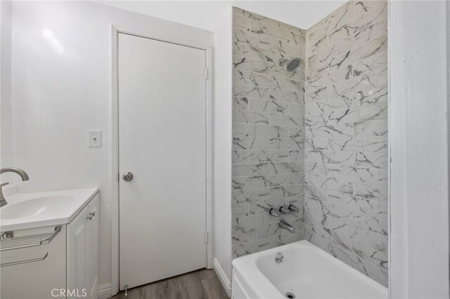 bathroom with wood-type flooring, vanity, and tiled shower / bath