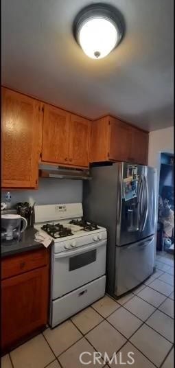 kitchen featuring dark countertops, brown cabinetry, white range with gas stovetop, stainless steel fridge, and under cabinet range hood