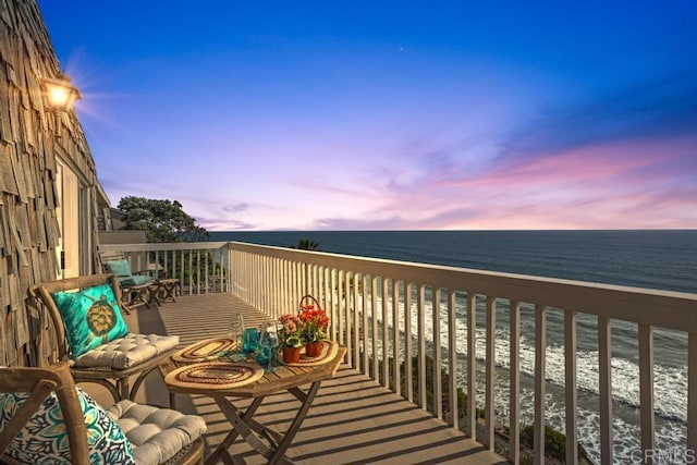 balcony at dusk featuring a water view