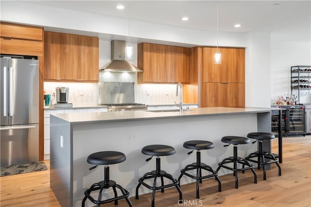 kitchen featuring hanging light fixtures, wall chimney exhaust hood, stainless steel appliances, and light wood-type flooring