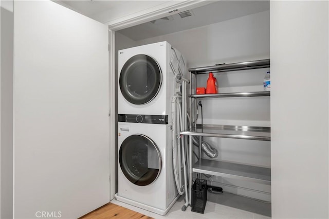 clothes washing area featuring hardwood / wood-style flooring and stacked washer / dryer