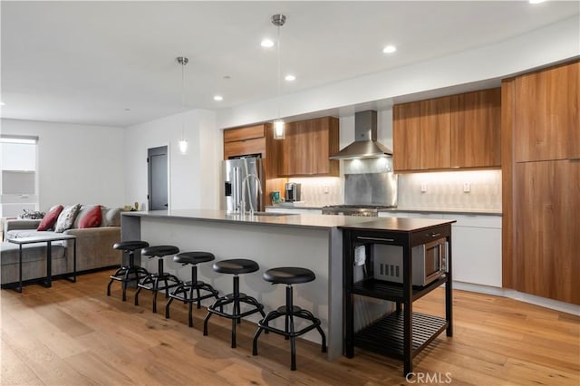 kitchen featuring sink, a center island with sink, wall chimney exhaust hood, and light wood-type flooring