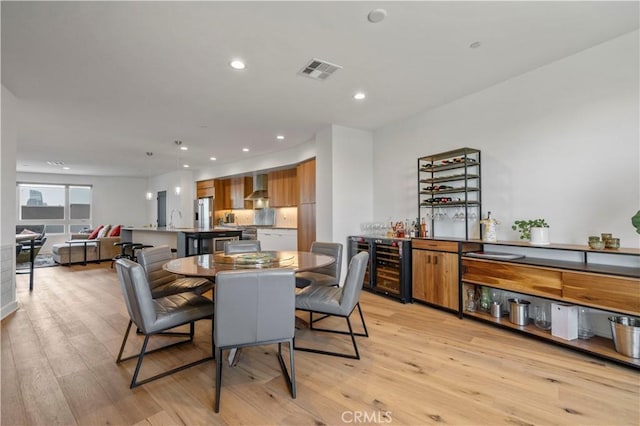 dining area with wet bar, beverage cooler, and light hardwood / wood-style flooring