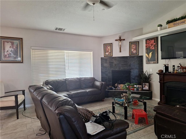 living room with a textured ceiling, ceiling fan, and a tiled fireplace