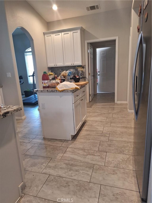 kitchen with backsplash, stainless steel fridge, white cabinets, and light stone countertops