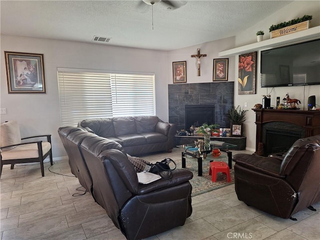 living room with a tiled fireplace, ceiling fan, and a textured ceiling