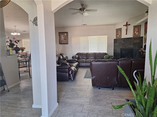 living room with a tile fireplace and ceiling fan with notable chandelier