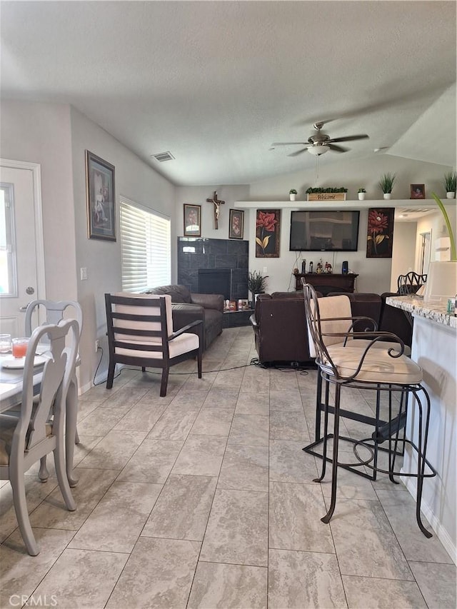 dining space featuring a textured ceiling, a stone fireplace, ceiling fan, and lofted ceiling