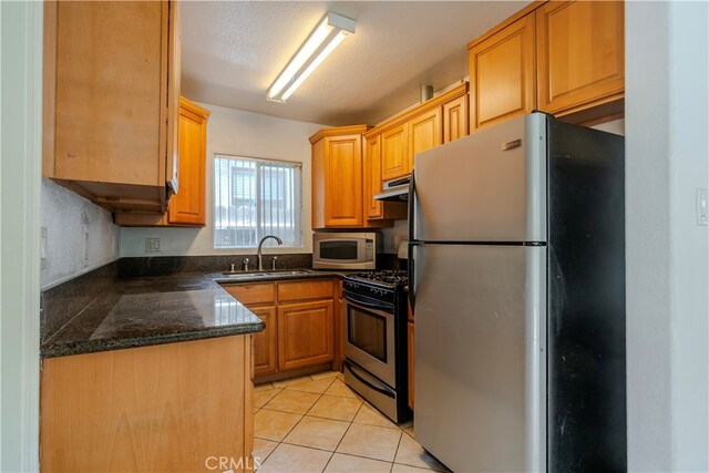 kitchen featuring sink, stainless steel appliances, a textured ceiling, light tile patterned floors, and dark stone counters