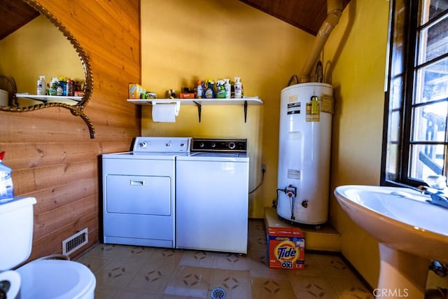 laundry room with water heater, wooden walls, sink, and independent washer and dryer