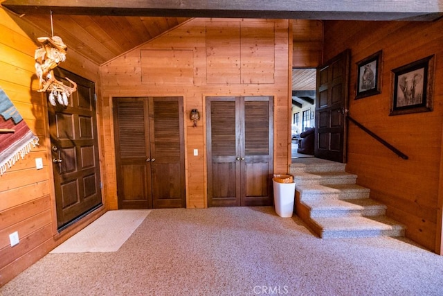 carpeted foyer featuring vaulted ceiling with beams and wood walls