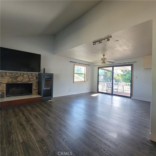 unfurnished living room with dark hardwood / wood-style floors, ceiling fan, a stone fireplace, and lofted ceiling