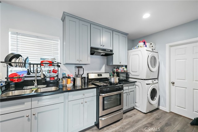 kitchen featuring gray cabinetry, stainless steel range with gas stovetop, stacked washer and dryer, hardwood / wood-style flooring, and sink