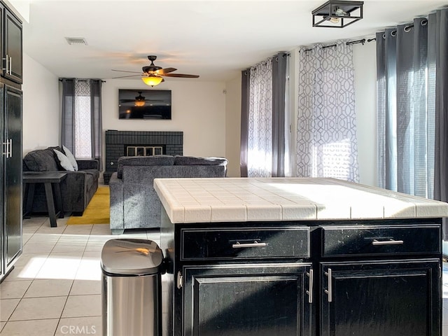 kitchen featuring ceiling fan, a kitchen island, light tile patterned floors, and a brick fireplace