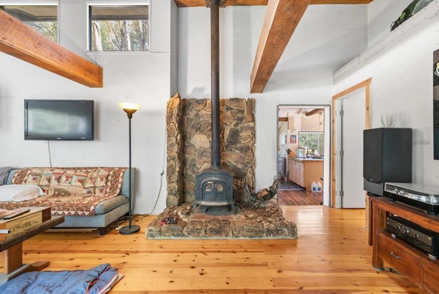 living room with plenty of natural light, beamed ceiling, a wood stove, and light hardwood / wood-style flooring