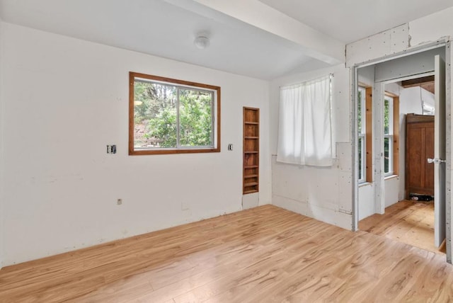 unfurnished room with light wood-type flooring and beamed ceiling