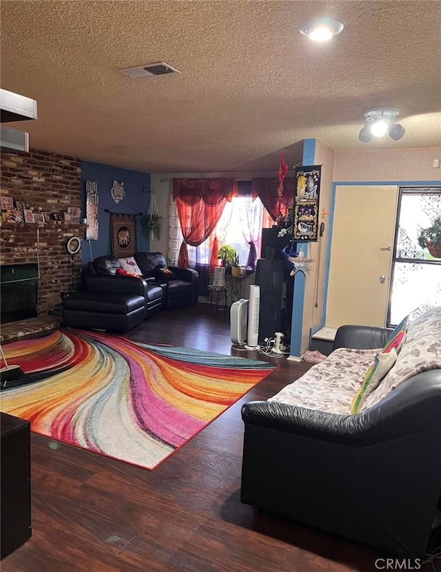 living room featuring a textured ceiling, hardwood / wood-style flooring, and a brick fireplace