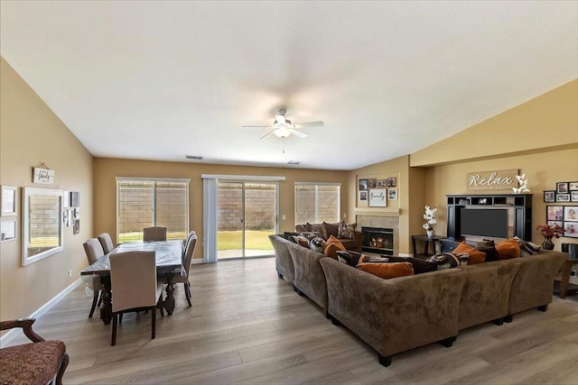 living room with ceiling fan, light hardwood / wood-style floors, lofted ceiling, and a tiled fireplace