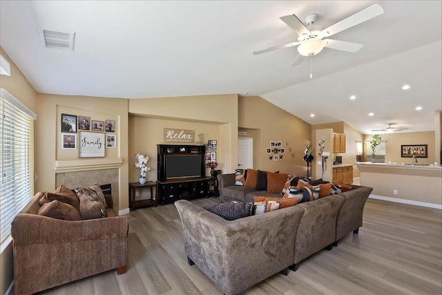 living room with wood-type flooring, vaulted ceiling, ceiling fan, and a tiled fireplace