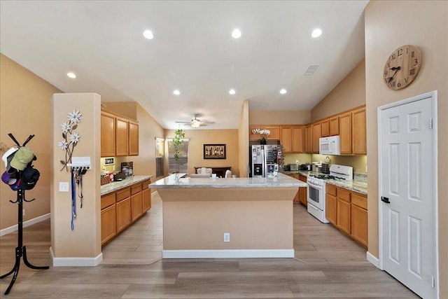 kitchen featuring ceiling fan, light hardwood / wood-style floors, vaulted ceiling, white appliances, and a center island with sink