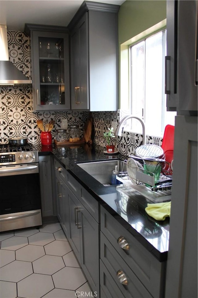 kitchen featuring tasteful backsplash, sink, wall chimney range hood, gray cabinets, and stainless steel stove