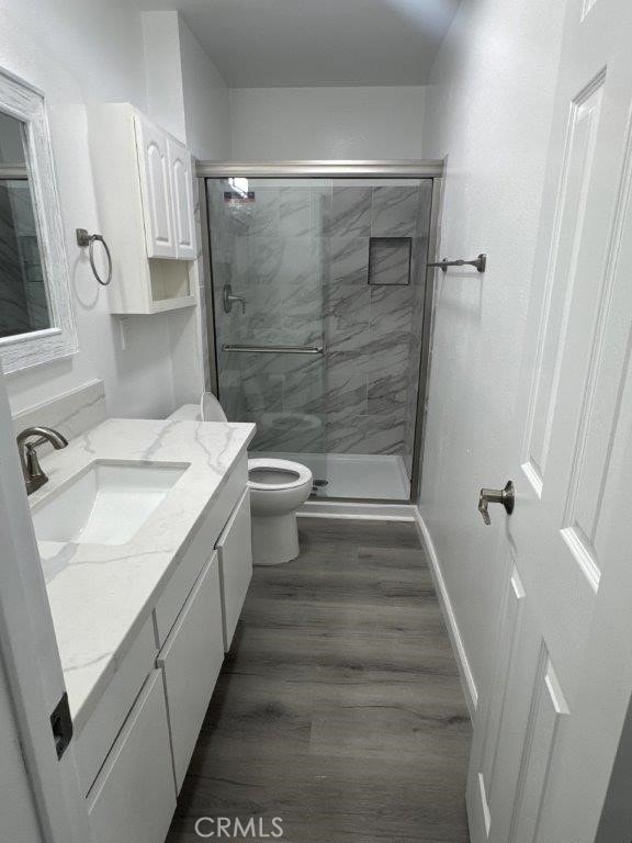 bathroom with a shower with door, hardwood / wood-style flooring, toilet, and vanity