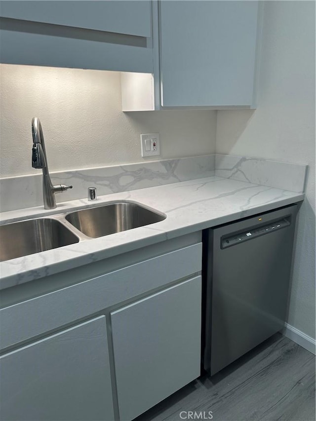 kitchen with light stone countertops, dishwasher, sink, and light hardwood / wood-style flooring