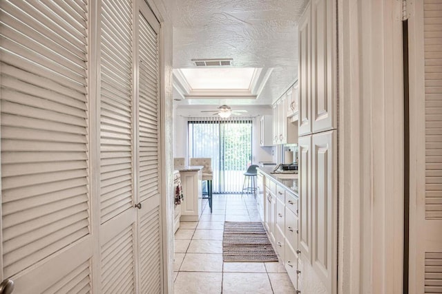 kitchen with white cabinets, light tile patterned floors, a textured ceiling, and a tray ceiling