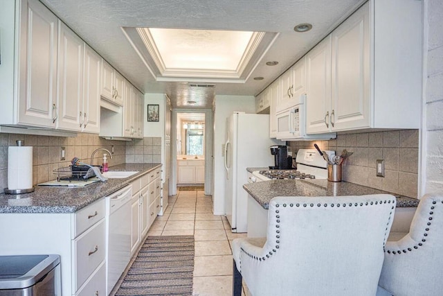 kitchen featuring white cabinetry, sink, white appliances, a tray ceiling, and light tile patterned flooring