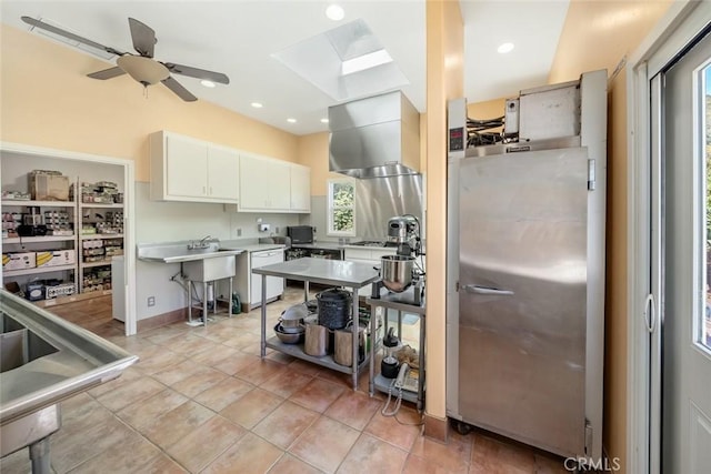 kitchen with light tile patterned floors, a skylight, white dishwasher, white cabinets, and a kitchen bar