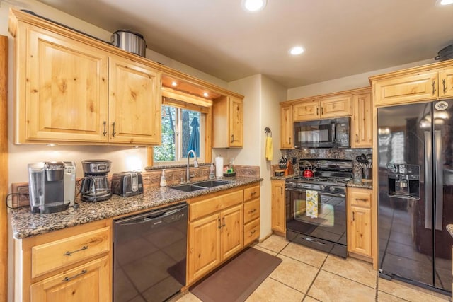 kitchen with dark stone countertops, light brown cabinets, light tile patterned floors, black appliances, and sink