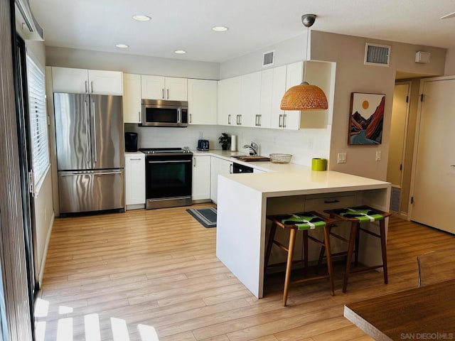 kitchen featuring white cabinets, appliances with stainless steel finishes, decorative light fixtures, and light hardwood / wood-style floors