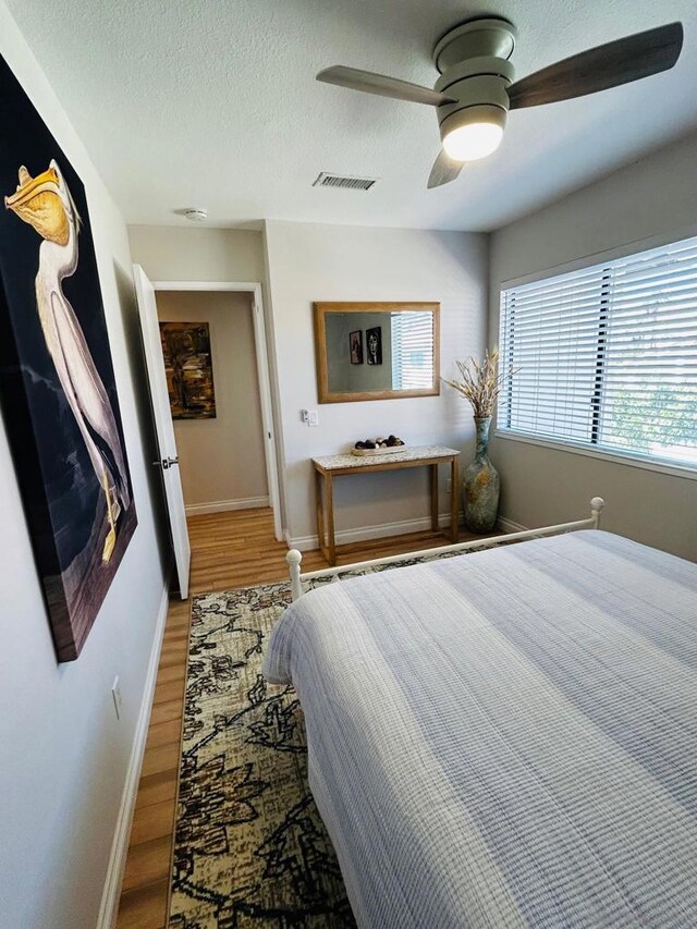 bedroom featuring ceiling fan, hardwood / wood-style floors, and a textured ceiling