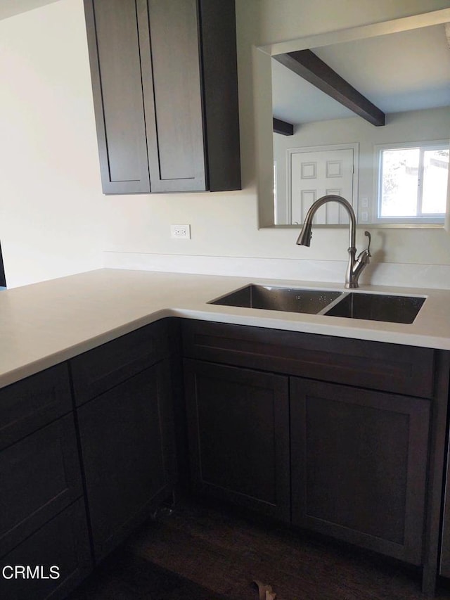 kitchen with dark brown cabinets, dark wood-type flooring, sink, and beamed ceiling