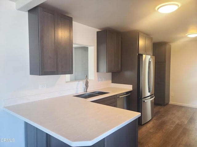 kitchen featuring kitchen peninsula, dark brown cabinets, sink, appliances with stainless steel finishes, and dark hardwood / wood-style flooring