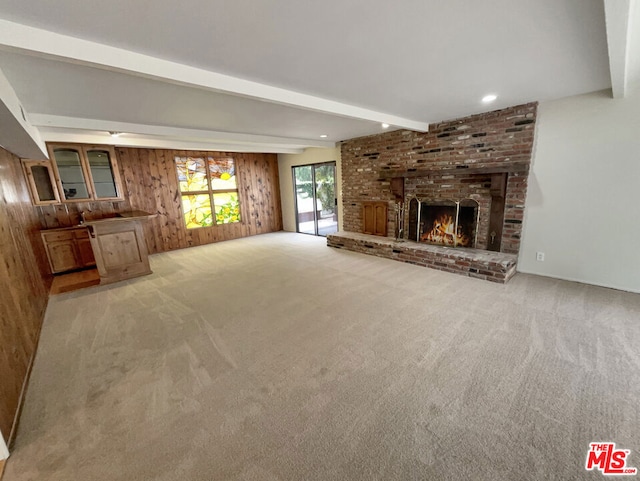 unfurnished living room featuring wood walls, beamed ceiling, light colored carpet, and a brick fireplace