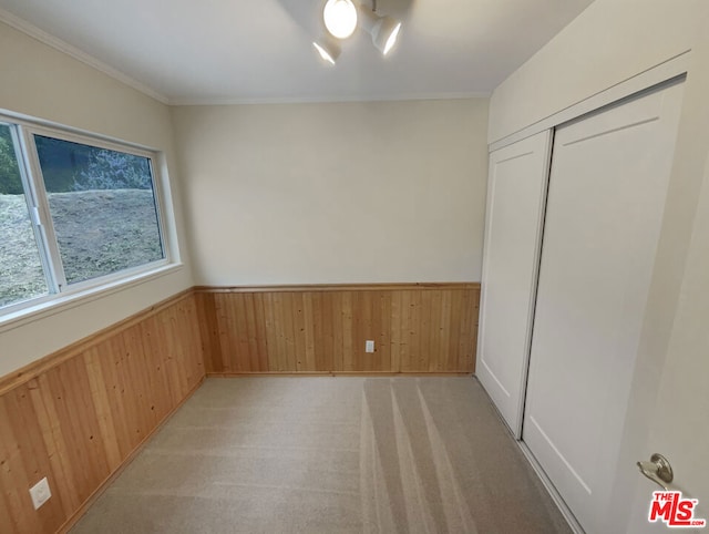 unfurnished bedroom with light colored carpet, crown molding, a closet, and wooden walls