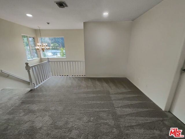 empty room featuring dark colored carpet and a notable chandelier