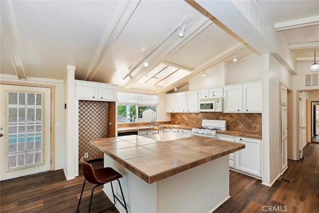 kitchen with white appliances, lofted ceiling with beams, dark hardwood / wood-style floors, a kitchen island, and white cabinetry