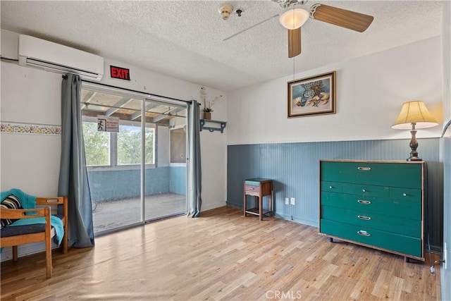 interior space featuring a textured ceiling, light hardwood / wood-style flooring, a wall unit AC, and ceiling fan