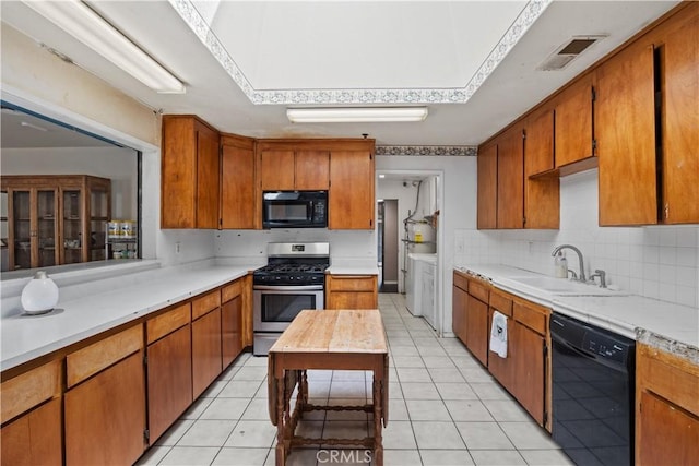 kitchen with washing machine and clothes dryer, sink, tasteful backsplash, light tile patterned floors, and black appliances