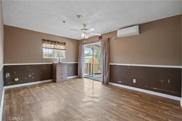 empty room with a wall mounted air conditioner, a textured ceiling, light hardwood / wood-style flooring, and ceiling fan