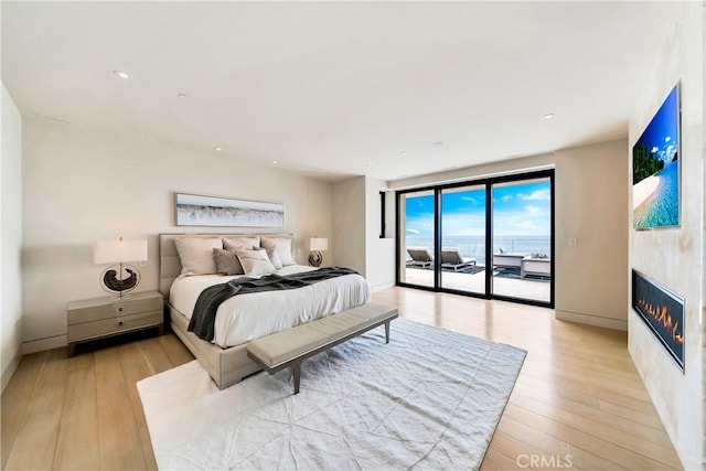 bedroom featuring access to outside, light hardwood / wood-style flooring, a water view, and a fireplace